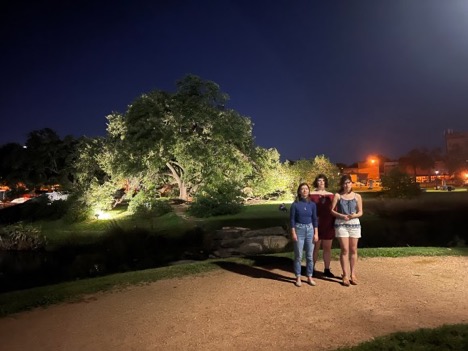 Three people singing at night. A large old tree and state hospital campus are in the background.